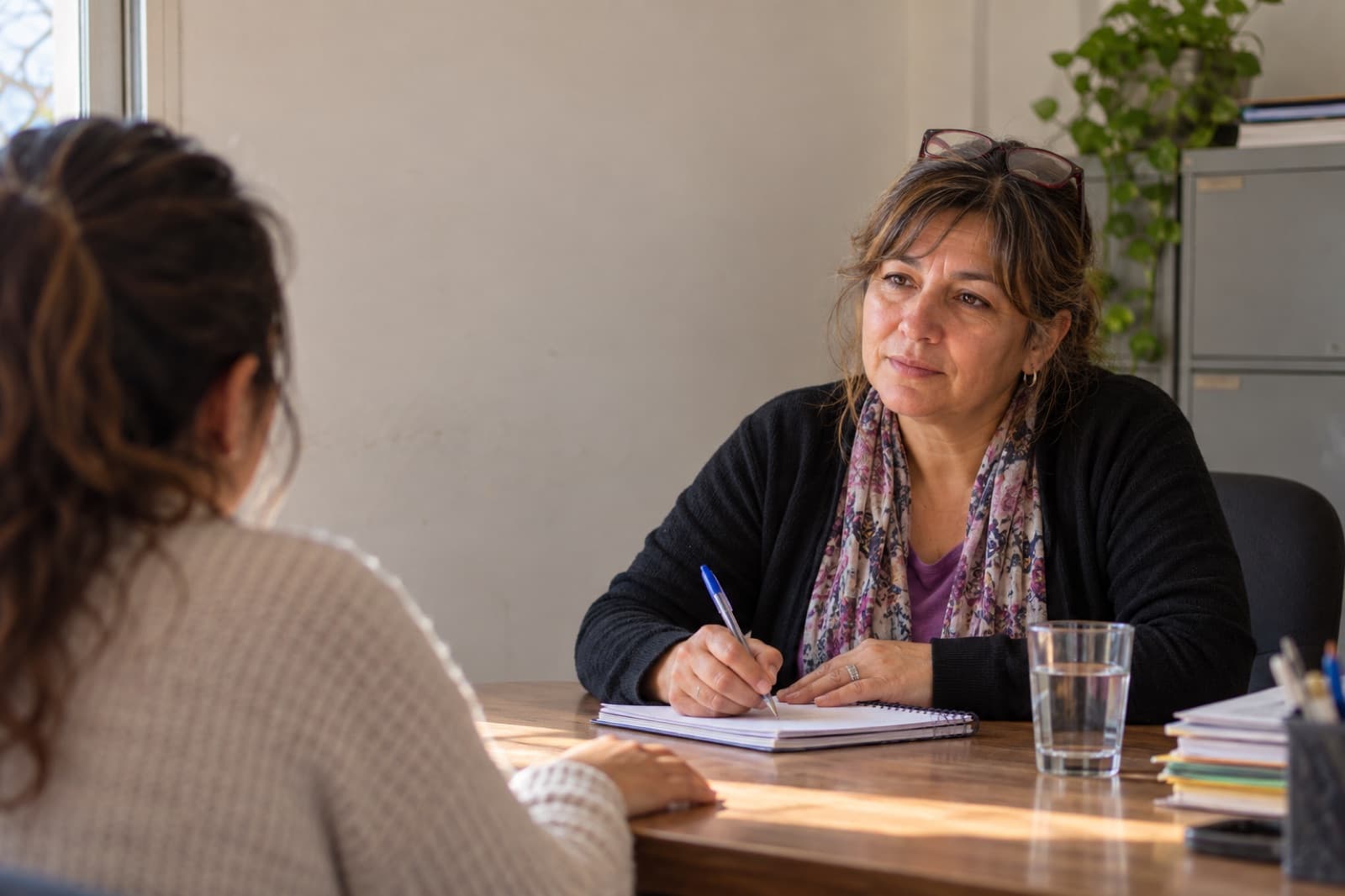 Una profesional del equipo escucha y toma notas frente a una mujer, que aparece de espaldas.